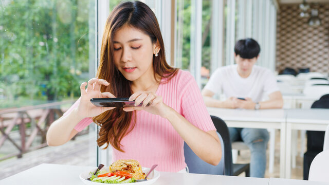 Young Asia female influencer food blogger taking photo of fried rice on smartphone, photographing meal with mobile camera in restaurant. Lifestyle new normal after corona virus and social distancing.
