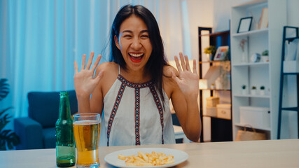 Young Asia lady drinking beer having fun happy night party New Year event online celebration via video call by phone at home at night. Social distance, quarantine for coronavirus. Point of view or POV