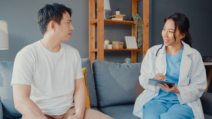 Fototapeta premium Young Asia female professional physician doctor using digital tablet sharing good health test news with happy male patient sit on couch in house. Medical insurance, Visit patient at home concept.