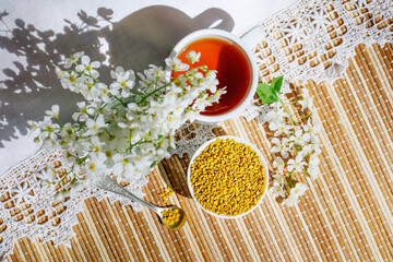 A bowl of pollen and aromatic herbal tea. Still life in a rustic style with a branch and flowers of a bird cherry and with a white knitted napkin. E