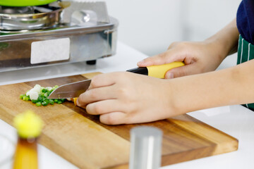 Cropped photo of kid learn to cook healthy food for family in modern home kitchen by using knife slice food on wooden plate into pieces.