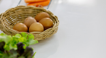 cleaned fresh chicken eggs in rattan basket beside vegetable on table of home kitchen prepared by mom as raw materials for teaching kid of family to cook healthy food