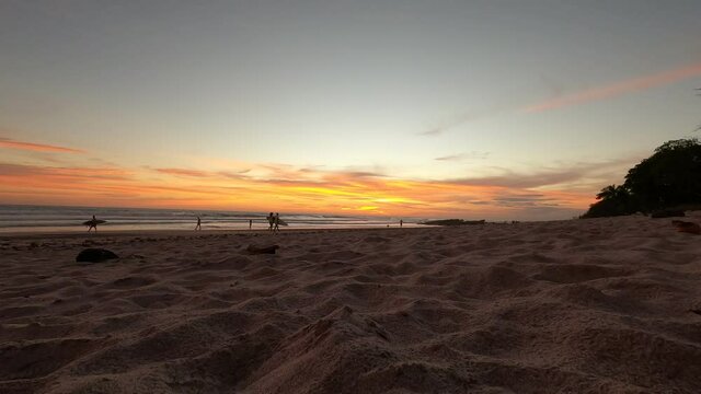 Time lapse of colorful sunset reflecting in the water with waves and surfers in the pacific ocean in Tamarindo, Costa Rica.