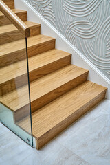 Wooden staircase with glass railings and wooden handrail of solid oak close view