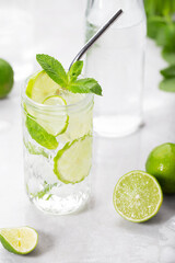 Mojito cocktail with lime and mint in a highball and a metal tube on background of light gray stone