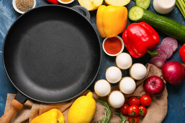 Clean frying pan with products on color background
