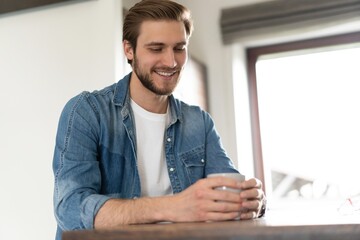 Young casual man with mug of tea or coffee in kitchen.