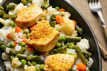 Frying pan with cooked vegetables, chicken and rice on table, closeup