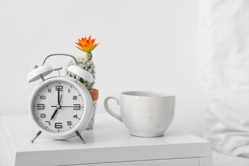 Alarm clock and cup on table near light wall