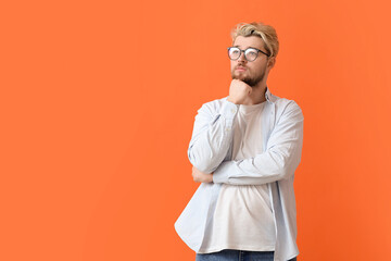 Thoughtful young man wearing eyeglasses on color background