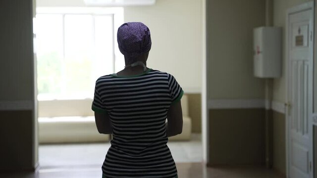 Woman with cancer with scarf on her head walks through the hospital ward.