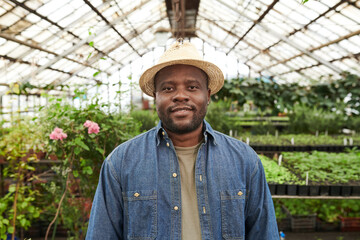 Obraz premium Portrait of African young farmer in hat looking at camera while working in the garden