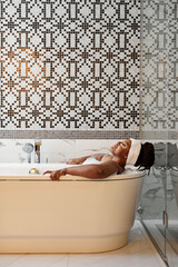 Relaxed African Woman Lying On Bathtub Enjoying Time Alone At Weekends, Hygiene Concept. Afro-american lady take bath, in bright modern cozy bathroom - obrazy, fototapety, plakaty