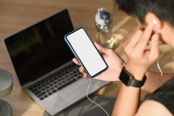 Sportsman listening to music with earphones and using mobile phone preparing for exercising at home.