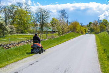 Man on a ride-on mower on a country road