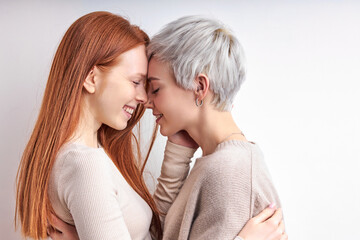 Side View Portrait Of Pretty Redhead Woman And Short Haired Lady Hugging, Feeling Love, Standing Closely To Each Other, Enjoying Time Together, Smiling Happily. LGBT, Lesbians, lgbt couple