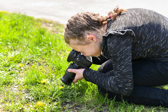 The girl takes a macro photo on a SLR camera in the park.