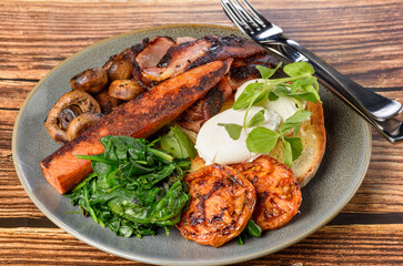 A serving of breakfast consisting of bacon, tomato, eggs, toast, mushrooms and spinach