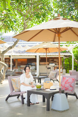 Beautiful woman tourist with white flower on her hair drinking coconut sitting on lounge chair during summer holidays