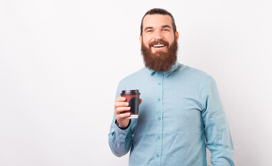 Naklejka premium A young bearded employee is smiling at the camera holding a cup of hot drink