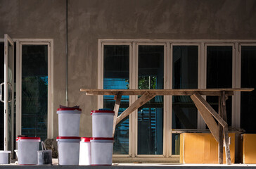 Front view of many mixing concrete polymer buckets and various material with wooden scaffolding inside of house construction site in loft style with evening mild sunshine