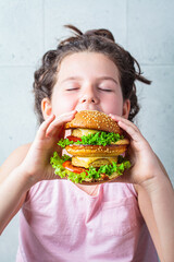 Brunette teenage girl eating big vegan burger.