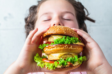 The child is eating big vegan burger, close-up.