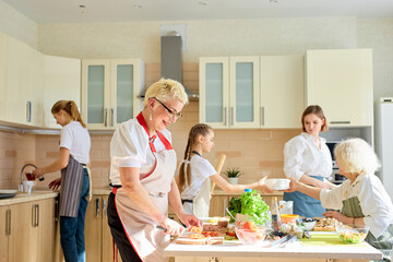 Smiling caucasian grandmother with children cooking together, having fun and talk while preparing meal. Food, cooking concept. Pretty women and kids at home in bright modern kitchen.
