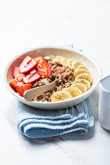 Buckwheat porridge with banana, strawberries and maple syrup in white bowl. Healthy breakfast concept.