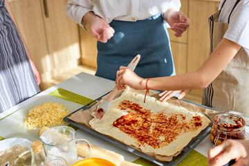 cropped female hand adding sause on pizza base, spreading tomato sauce with lubricator, preparing for baking, preparing tasty pizza together. At home, in kitchen. domestic atmosphere