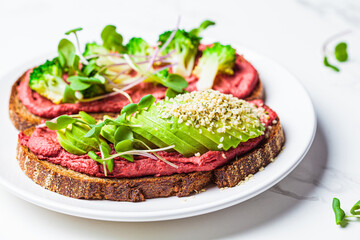 Toasts with beetroot hummus, avocado and broccoli, white marble background. Vegan food concept.