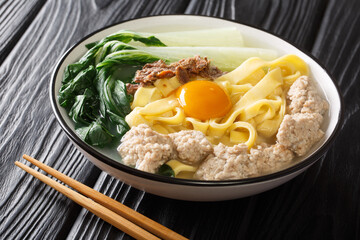 Delicious Asian homemade noodle soup with fried anchovies, meatballs and bok choy close-up in a bowl on the table. horizontal