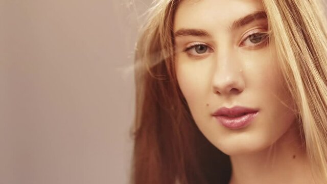 Natural beauty. Romantic woman. Enjoying moment. Sunshine glow. Sensual blonde woman with long fair hair looking at camera wind blow isolated beige blur lens flare copy space slow motion.