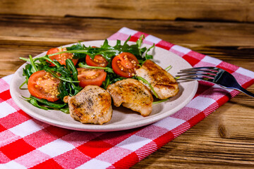 Roasted chicken breasts and salad with arugula and cherry tomatoes in a ceramic plate