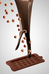 melted chocolate is poured into a chocolate mold mixed with hazelnuts on a light background. Making...