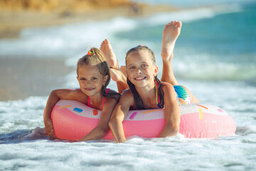 Obraz premium Children are playing on the beach. Children swim and play in the sea on summer family vacations. Sand and water activities. Two girls run on the ocean shore. High quality photo.