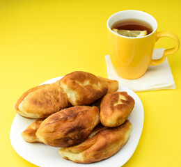 Lemon tea in a yellow ceramic mug and fried homemade pies on a white plate, on a yellow background. The concept of a hearty breakfast and snack. Top and side view.