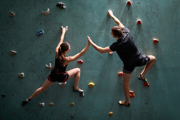 Friendly man and woman give high five to each other while climbing the rock together, rear view on...