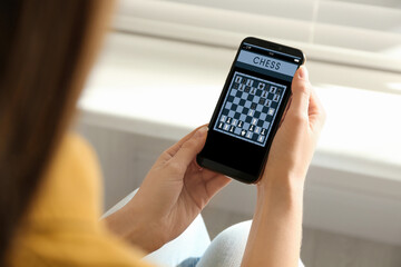 Woman playing online chess on smartphone indoors, closeup