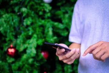 Man holding smartphone with christmas tree background, Technology concept.