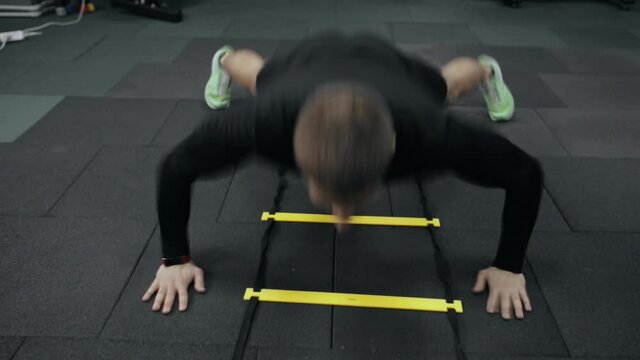Strong athletic man doing push ups exercise on speed agility ladder during active training in gym 