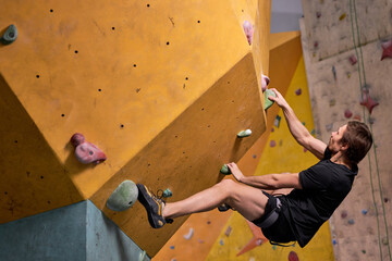 Young Man Climbs Up An Artificial Rock Wall,Sport And Fitness Concept, Side View. Fit Athlete Guy...