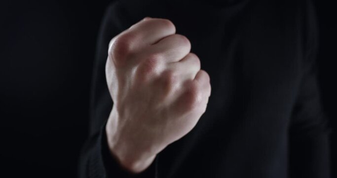 Angry man threatens with index finger and threatens with his fist. Dangerous man demands submission and threatens with violence on black background. Terrible boss requires monitoring and subordinated