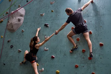 Fotobehang two Athletes climber moving up on steep rock, climbing on artificial wall indoors together supporting and helping, in sportive outfit. Extreme sports and bouldering concept © Roman