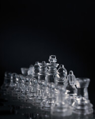 Vertical shot of transparent glass chess pieces on a board isolated on black background