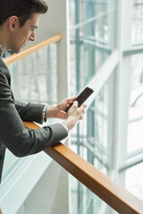 Close-up of young businessman talking online on mobile phone while standing on the balcony