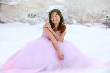 Fototapeta na wymiar Teen girl in pink formal gown sitting outdoors in snow