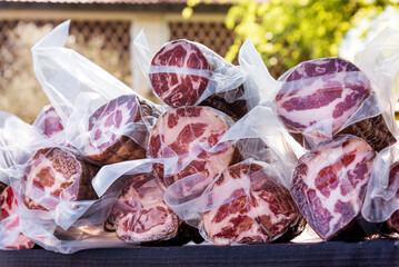 Display of vacuum packed cured coppa ham outdoors at market
