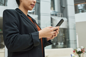 Close-up of businesswoman typing a message on her mobile phone while standing in the city