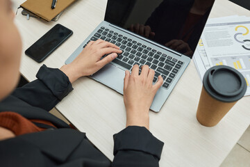 Close-up of office worker typing on laptop computer and drinking coffee during her work at office